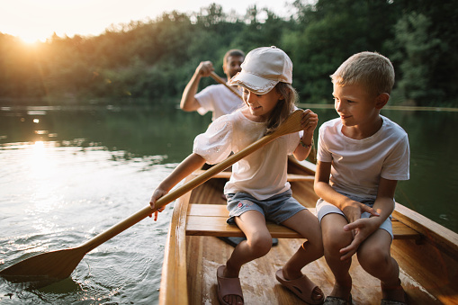 Family time, brother and sister learning to paddle canoe with father