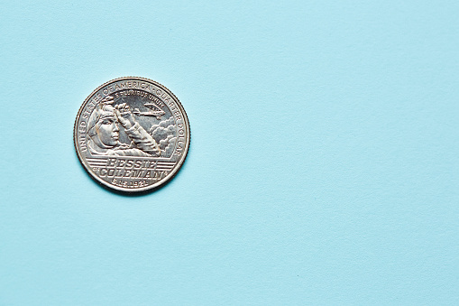Close-up of an American quarter, commemorating the aviator Bessie Coleman, on a textured paper background in light blue.