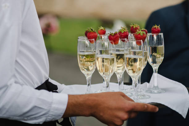 il cameriere serve e porta un vassoio con bicchieri di champagne e fragole. concetto di festa e celebrazione delle vacanze. concetto di servizio di ristorazione. una donna tiene in mano lo spumante. primo piano. - party business toast champagne foto e immagini stock