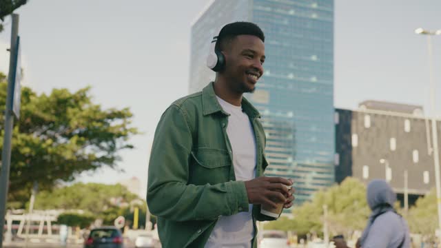 Young black man in casual clothing smiling while hitchhiking with headphones and coffee on street