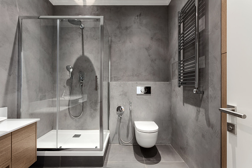 modern interior in hotel bathroom, shower cabin with glass door, wall mounted toilet with concealed cistern tank and stainless steel heated radiator