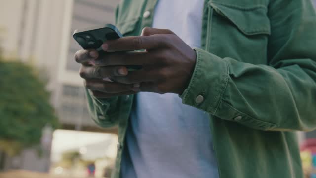 Close-up of young black man in casual clothing scrolling on mobile phone in street