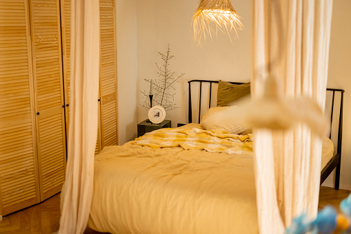 Interior view of bedroom in beige tones with straw lampshade and wardrobe shutters. Boho style natural materials