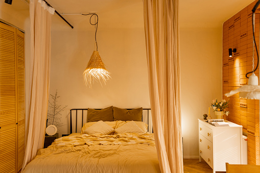 Interior view of bedroom in beige tones with straw lampshade and canopy. Boho style natural materials