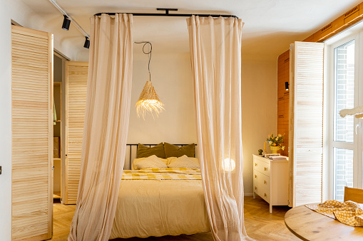 Interior view of bedroom in beige tones with straw lampshade and wardrobe shutters. Boho style natural materials