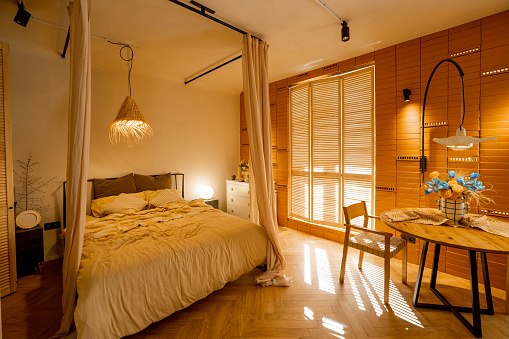 Interior view of bedroom in beige tones with straw lampshade and canopy. Boho style natural materials