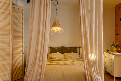 Interior view of bedroom in beige tones with straw lampshade and wardrobe shutters. Boho style natural materials