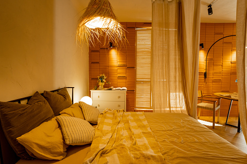 Interior view of bedroom in beige tones with straw lampshade and brick wall. Boho style in natural materials