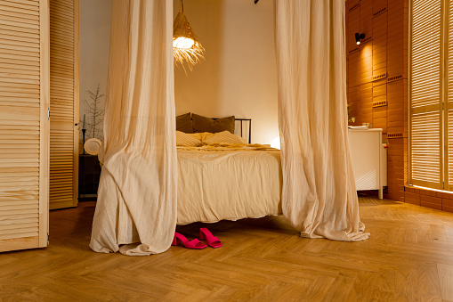Interior view of bedroom in beige tones with straw lampshade and canopy. Boho style natural materials