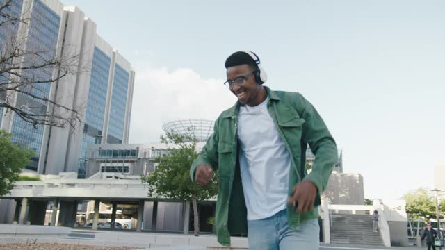 Happy young black man in casual clothing with wireless headphones dancing in street