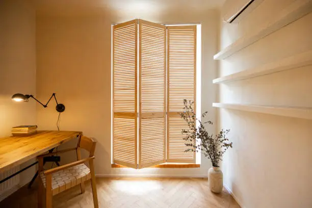 Interior view of workspace with wooden table and chair near the window with shutters in stylish studio apartement