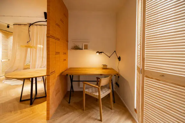 Interior view of workspace with wooden table, chair and lamp in stylish studio apartement