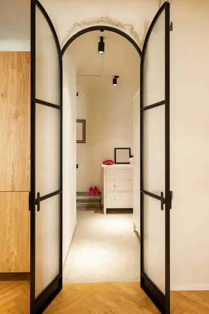 View through the metal glass door on the hallway of modern studio apartment in white tones