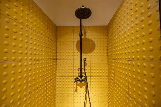 Shower cabin made with yellow tactile tiles with a black faucet