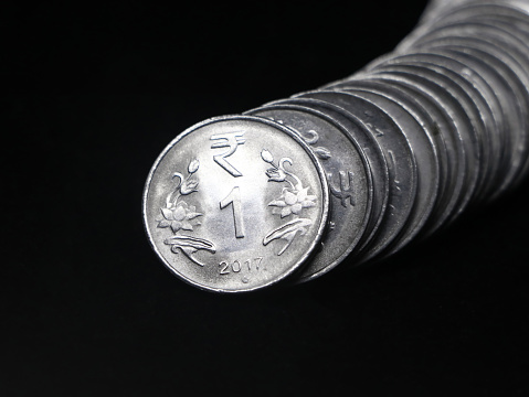 1 (one) rupee coins of india made of silver stacked together in a curved row shaped like a snake in closeup isolated in a black background
