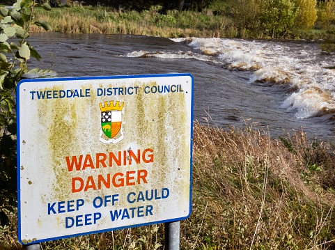 An old quaint sign next to River Tweed in Scottish Borders warning of cold deep water