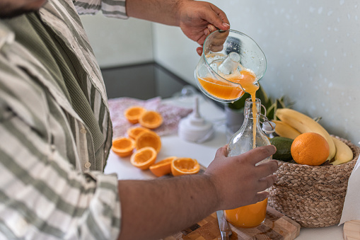Pouring fresh orange juice in reusable glass bottle