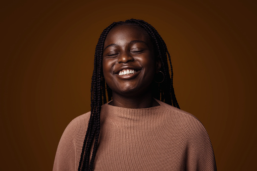 Portrait of a happy young adult woman/teenager against a dark brown background.