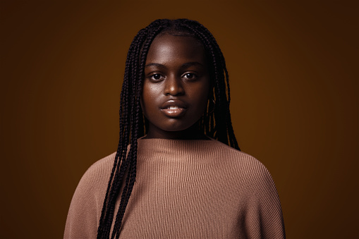 Portrait of a serious young adult woman/teenager against a dark brown background.