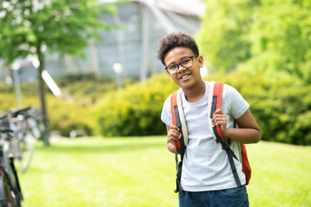 istock Schoolboy with backpack wearing white shirt standing in green park. 1504354071