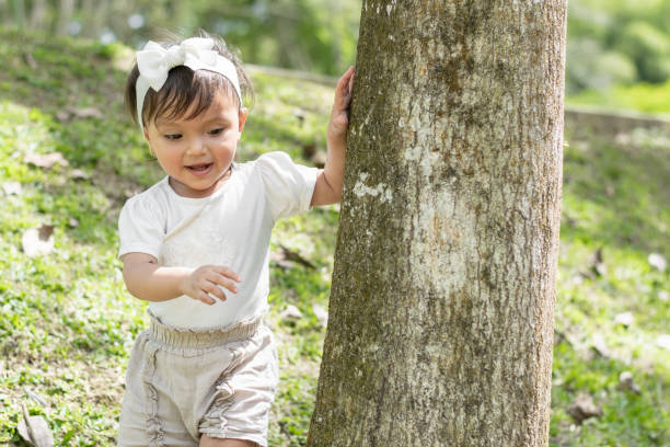 beautiful little brunette girl, playing around a large tree, surrounding it while smiling happily