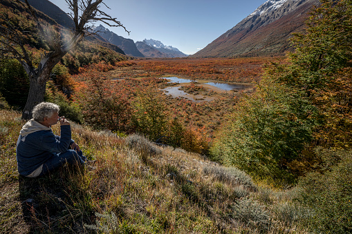 Adult man drinks a tea sitting on the grass while contemplating the incredible landscape. In the area of El Chalten, Santa Cruz, Argentina.