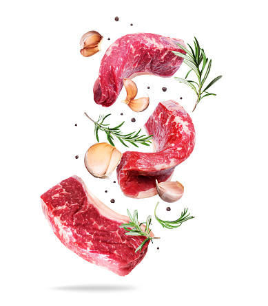 Three raw beef steaks with rosemary and garlic cloves isolated on a white background
