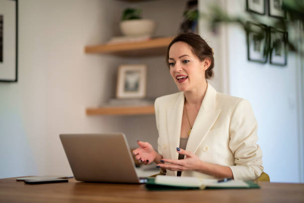 Smiling young businesswoman with laptop sitting at home and having video conference stock photo