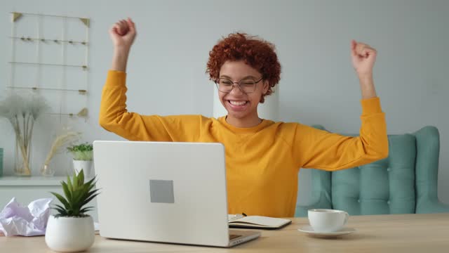 Excited happy african american woman winner. Girl female student looking at laptop passed exam reading great news getting good result winning online bid feeling amazed looking at computer at home.