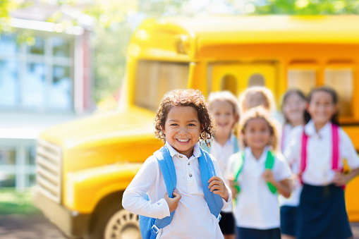 Kids go back to school on bus. Interracial group of children of mixed age run and cheer on the first day of new academic year. Start of holiday. Preschooler or kindergarten kid. Child in school yard.