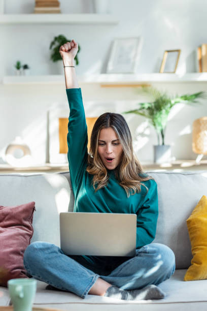 istock Pretty young woman celebrating something while using her laptop on the sofa at home. 1504462183