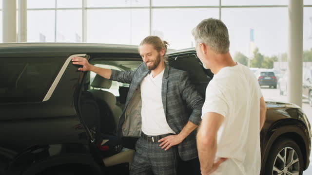 Middle aged grey haired man and his adult son trying out new baby seat in car dealership. Two men elderly father and adult son in a showroom choose a new car. Man chooses auto. Sales concept.