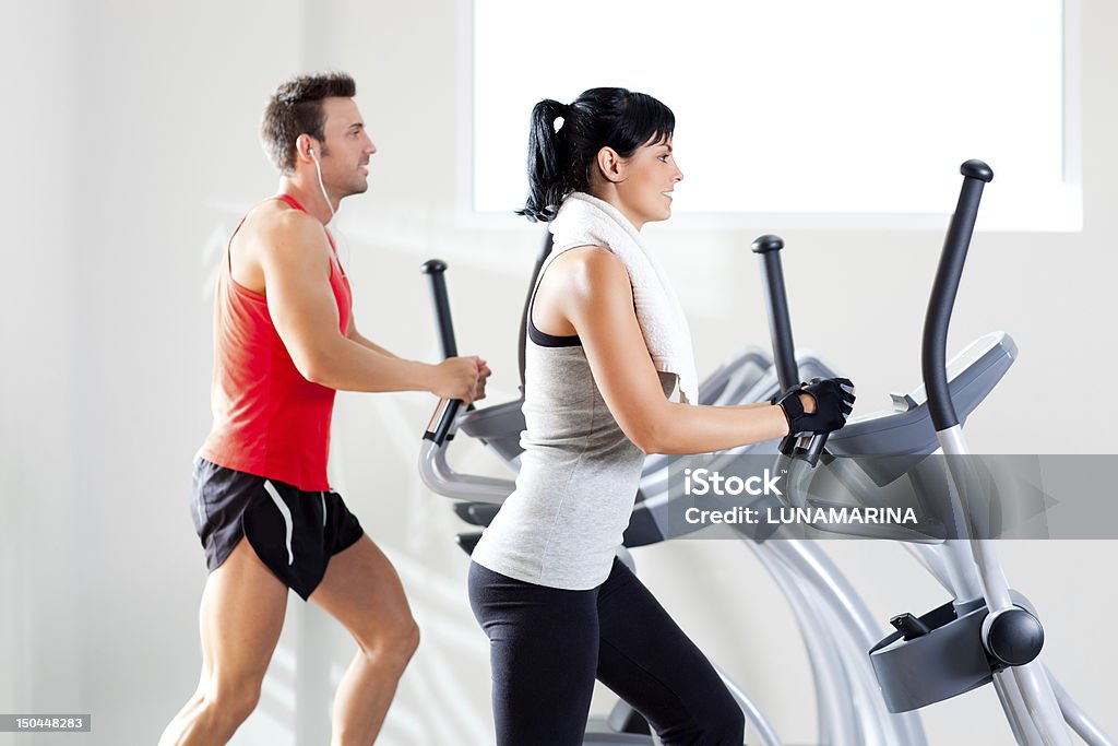 A man and woman using elliptical machines at the gym man and woman with elliptical cross trainer in sport fitness gym club 20-24 Years Stock Photo