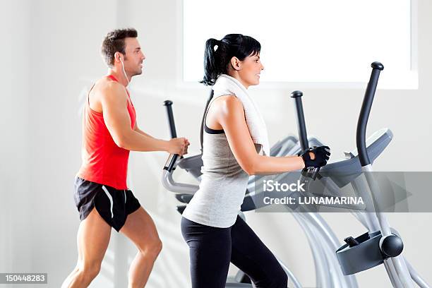 A Man And Woman Using Elliptical Machines At The Gym Stock Photo - Download Image Now