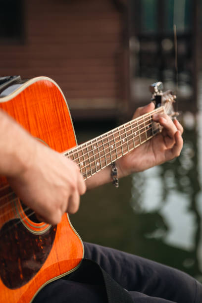 mężczyzna gra na gitarze, siedząc na drewnianym molo w pobliżu jeziora. - playing an instrument vertical blurred motion outdoors zdjęcia i obrazy z banku zdjęć