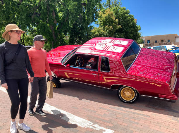 Santa Fe, NM: Tourist couple walk past a tilted lowrider car on the historic Santa Fe Plaza on the annual (June) Lowrider Day.
