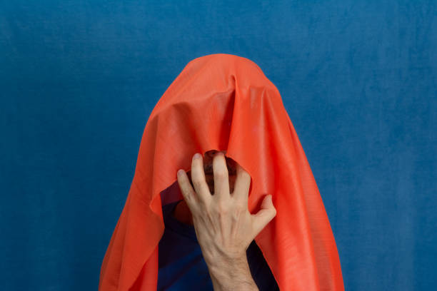 Man completely covering his head with an orange cloth and with one hand in front. Isolated on blue background.