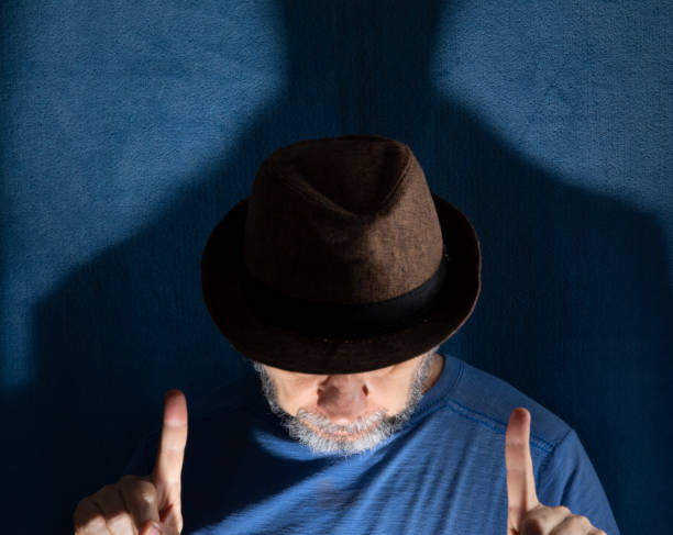 Studio portrait of man wearing hat with head down and gesticulating. Isolated on blue background.