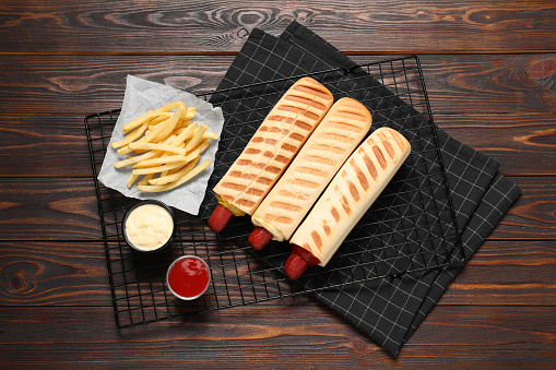 Delicious french hot dogs, fries and dip sauces on wooden table, top view