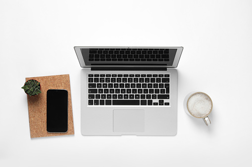 Laptop, smartphone, houseplant and cup of coffee on white background, flat lay