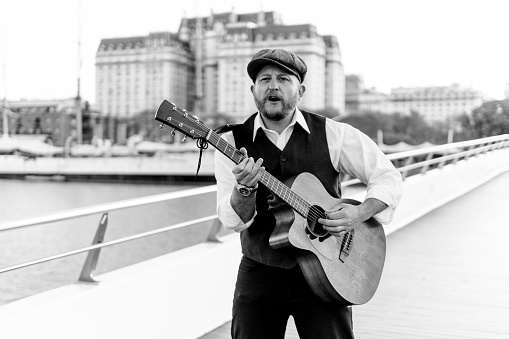 Black and white portrait of a musician playing the guitar and singing on a bridge over a river