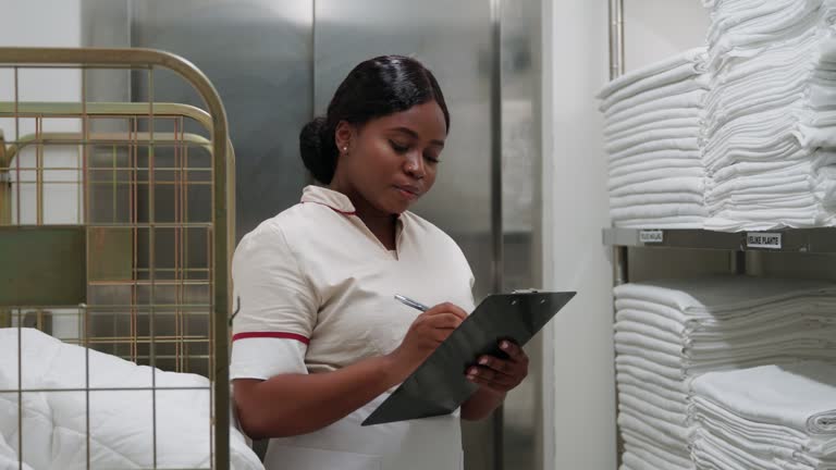 Uniformed African-American maid checking clean bed sheets