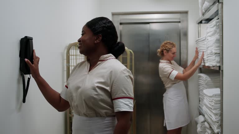 African-American maid answering staff phone while working in laundry with Caucasian colleague