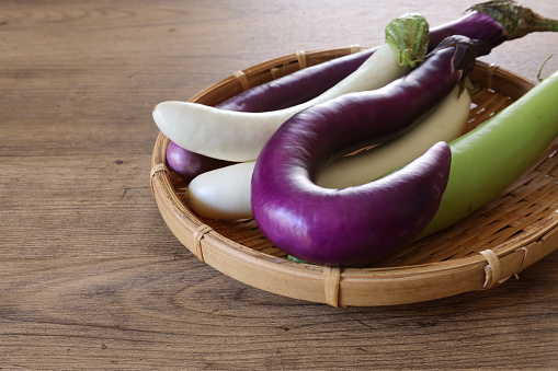 Elongated eggplants on a bamboo colander isolated on a wooden table.