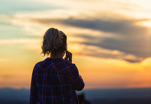 Woman using a smart phone while enjoying the sunset on the top of a mountain