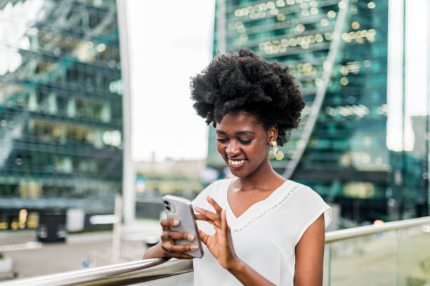 istock Young adult black woman using mobile with skyscrapers at background 1504597151