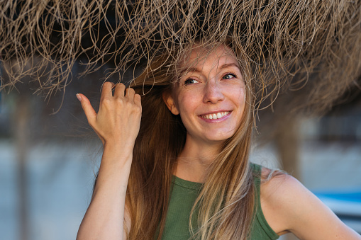Candid portrait of smiling young caucasian woman touching her hair looking sideways.