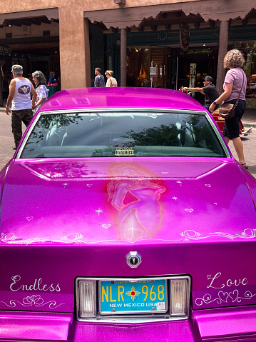 Santa Fe, NM: Tourists walk past a vibrant pink lowrider car on the historic Santa Fe Plaza on the annual (June) Lowrider Day.