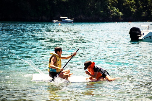 Two boys in life jackets on  paddle boards. Taken in the coastal waters of the Marlborough Sounds, New Zealand.