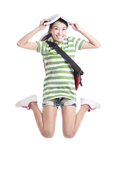 Excited student girl jumping with book Excited student girl jumping with book and bag in full length - isolated over white background, model are asian people school sport high up tall stock pictures, royalty-free photos & images